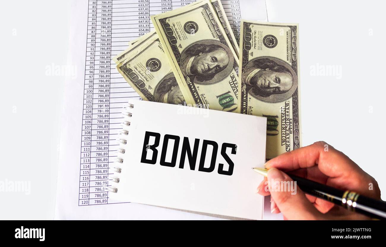 The word Bonds on a notebook is written with a pen by a female hand. Dollar banknotes and documents on a white background Stock Photo
