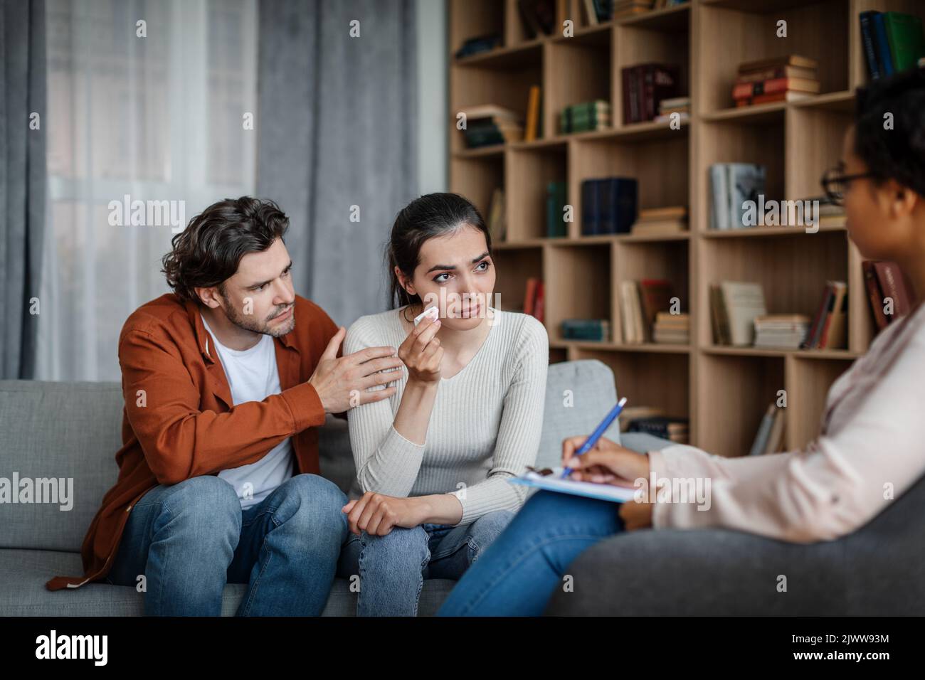 Unhappy sad millennial caucasian man calms crying woman at meeting with psychologist in office Stock Photo