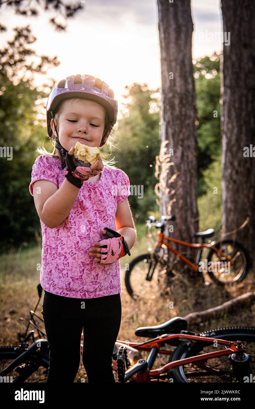 a little girl standing in front of the bicycle eat an apple Stock Photo