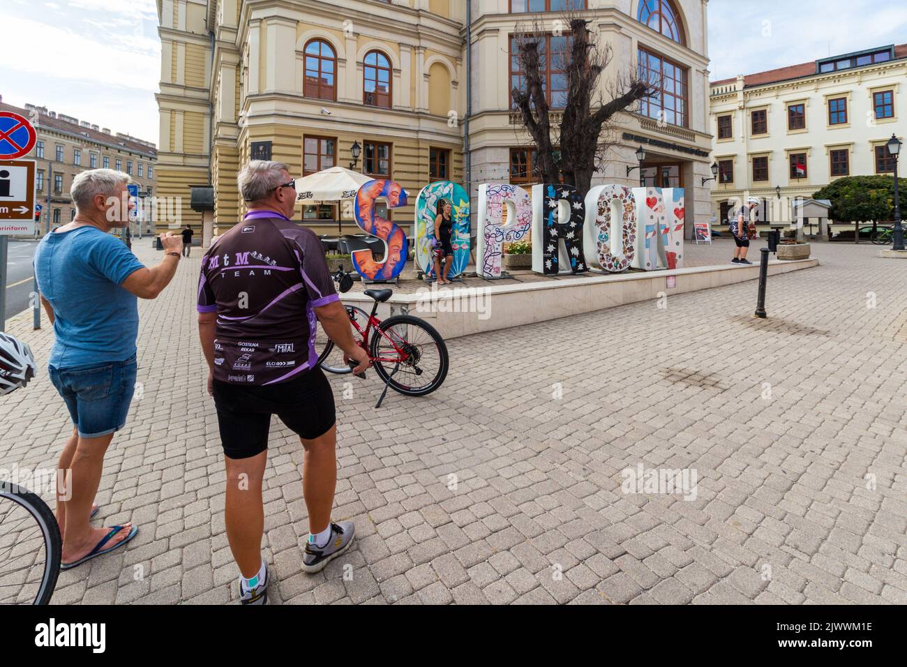 Cyclist tourists taking photos in Szechenyi ter in front of big SOPRON word, Sopron, Hungary Stock Photo