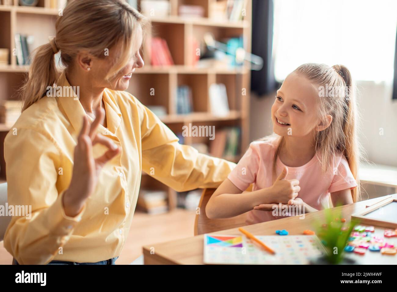 Positive teacher making hand gesture practice nonverbal talk with girl child, tutor learn sign language with small kid Stock Photo