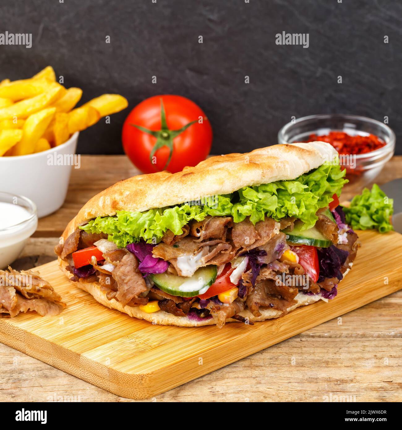 Döner Kebab Doner Kebap fast food meal in flatbread with fries on a wooden board square board Stock Photo