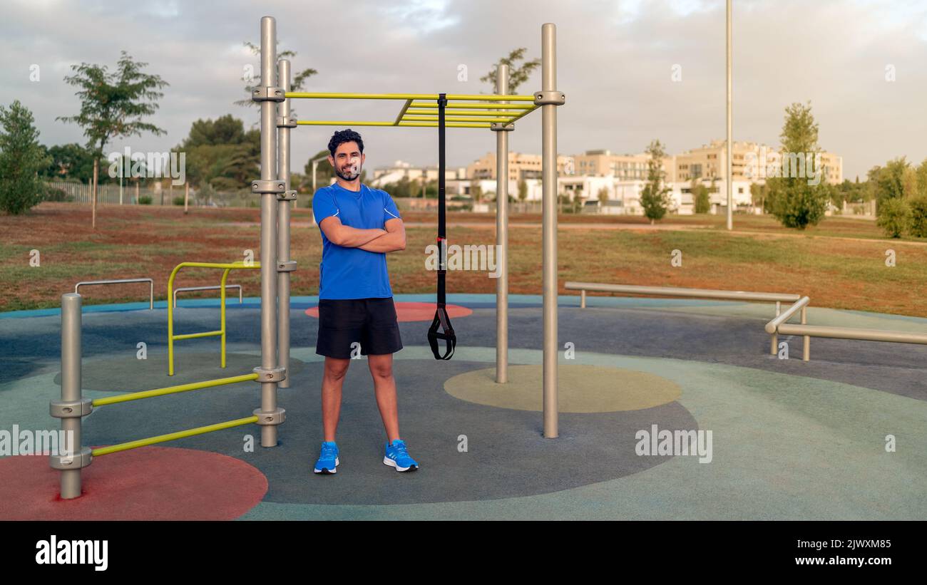Portrait of confident caucasian man exercising outside in sunny park. Great TRX workout. Young handsome guy in sportswear doing exercising outdoors. H Stock Photo