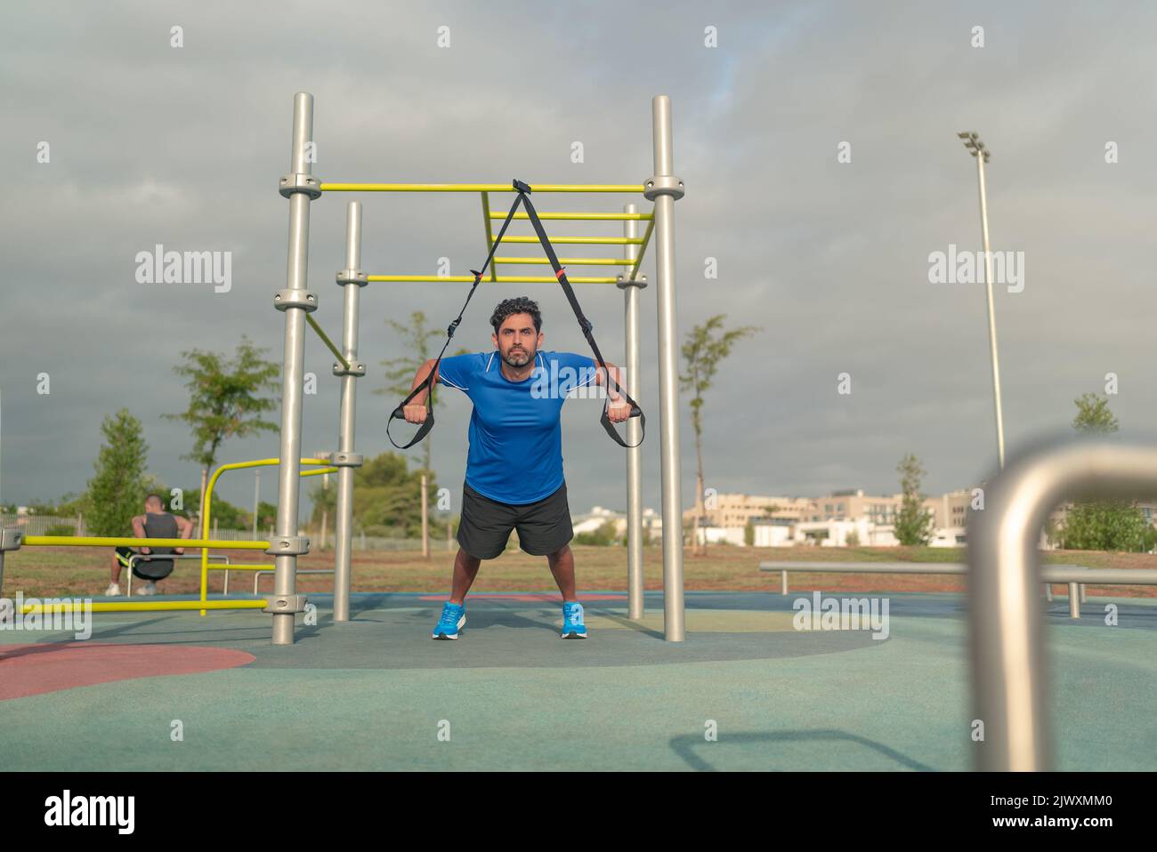 Caucasian man exercising outside in sunny park. Great TRX workout. Young handsome guy in sportswear doing exercising outdoors. Healthy lifestyle conce Stock Photo