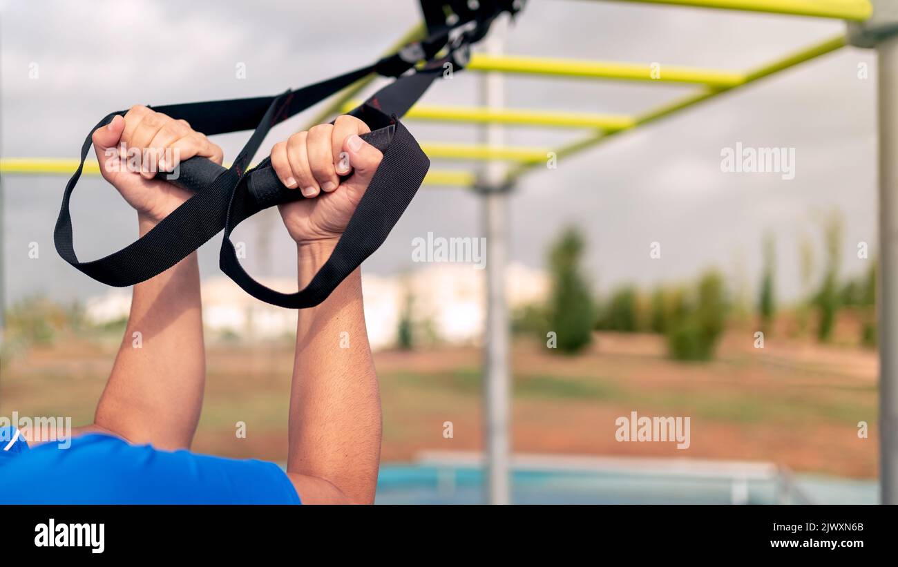Close up hands of young man doing fitness exercises on a special hanging device. Fitness male guy doing exercising with suspension trainer slingin a c Stock Photo