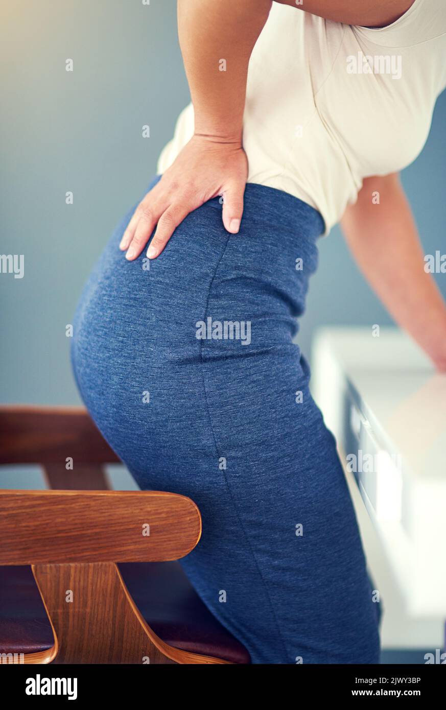 The effects of sitting for too long. a young businesswoman holding her