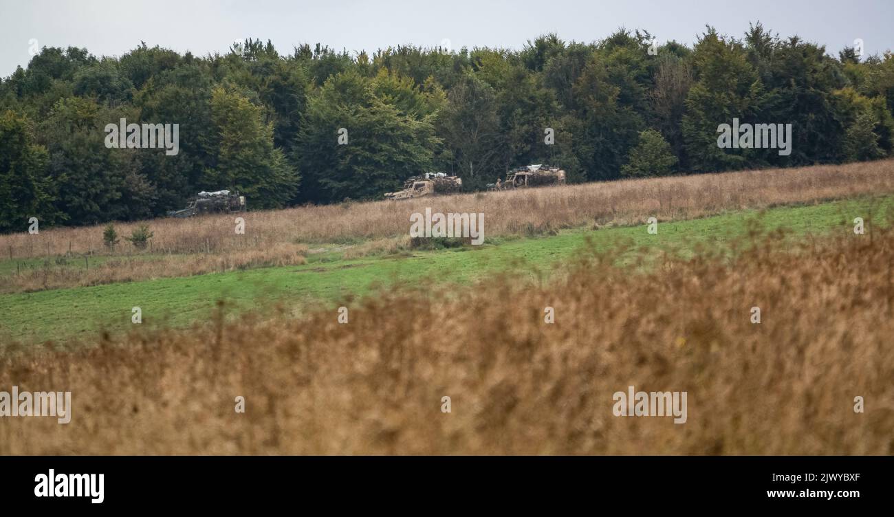 Three British army Foxhound light protection patrol vehicles (LPPV Force Protection Ocelot) taking cover behind woodland on a military exercise Stock Photo