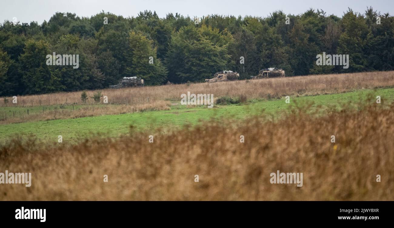 Three British army Foxhound light protection patrol vehicles (LPPV Force Protection Ocelot) taking cover behind woodland on a military exercise Stock Photo