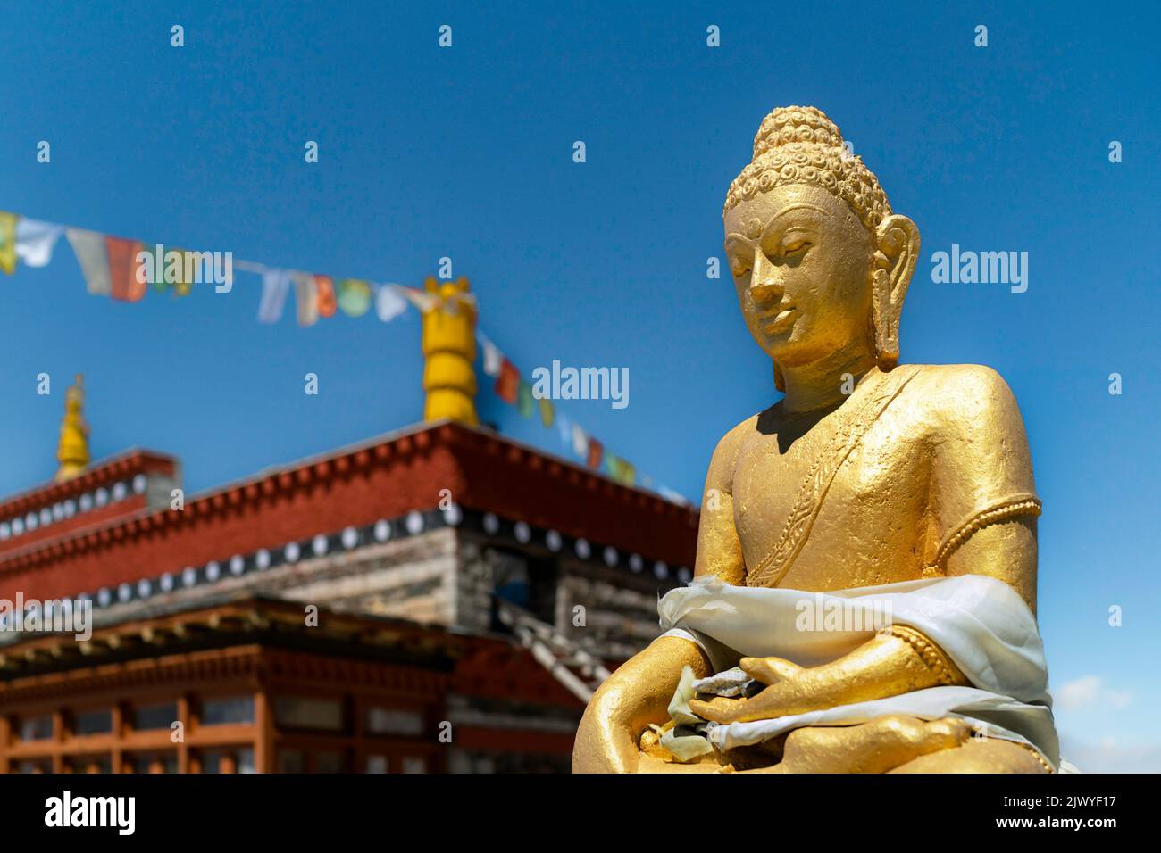 Gold pained statue of meditating Buddha in sitting position against a bright blue sky in the small Himalayan village of Nako, Himachal Pradesh, India. Stock Photo