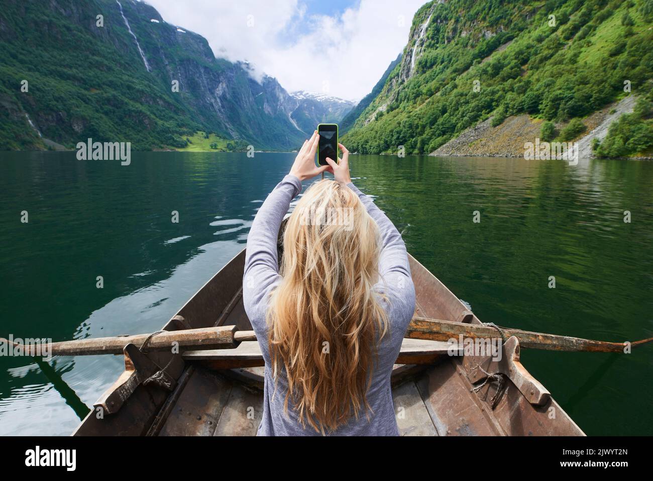 Adventure woman in row boat taking photo on smart phone of beautiful fjord lake for social media Stock Photo