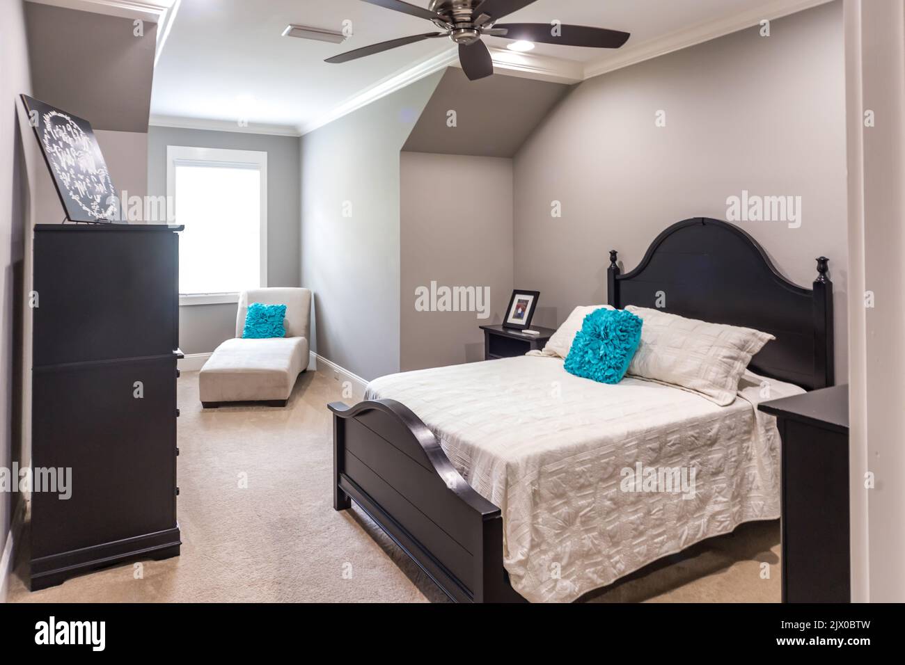 A spacious bedroom with a dark wood bed and dresser or chest and a fan and chaisse chair. Stock Photo
