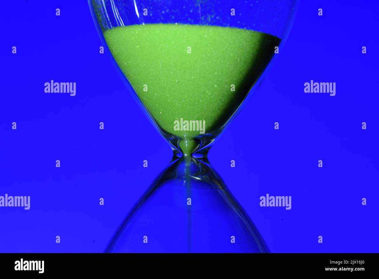 Detalle de un reloj de arena de color verde, contando el tiempo, sobre diferentes fondos Stock Photo
