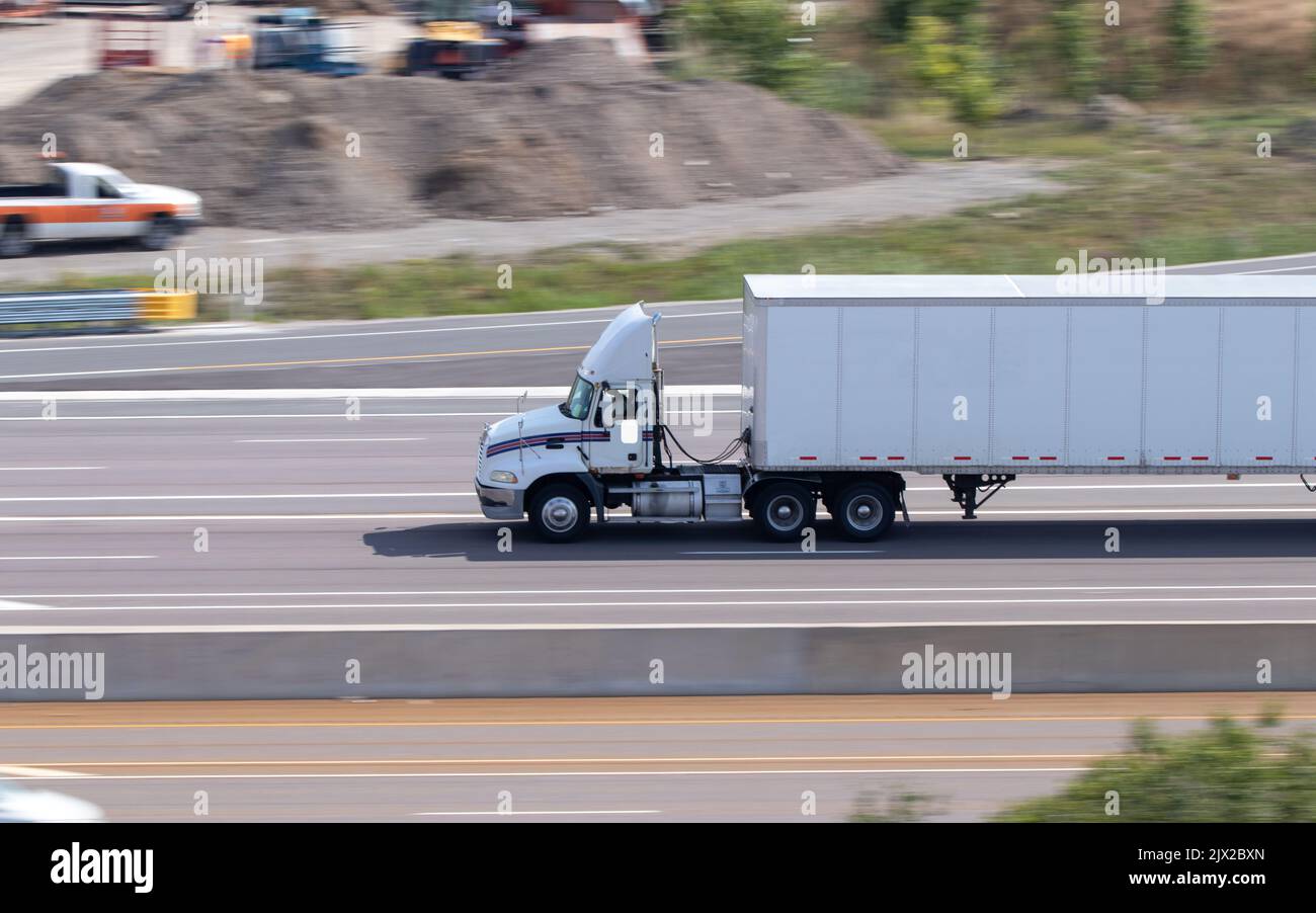 A blank, white semi-truck and trailer is seen on a multi-lane highway on a sunny day. Stock Photo