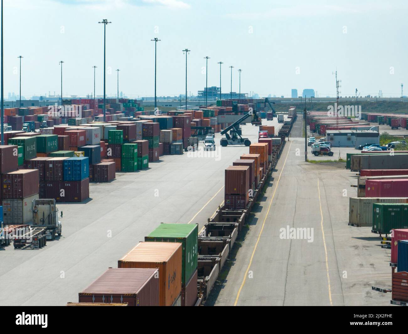 An aerial photo above a shipping terminal while a freight train is seen stopped in the terminal, being loaded in with shipping containers during day. Stock Photo