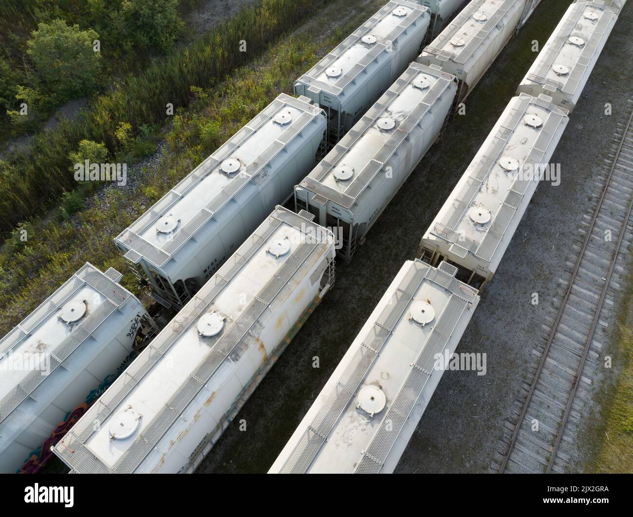 An aerial photo above a railyard with rows of covered hopper train cars stationary, parked near a coal mining and processing facility. Stock Photo