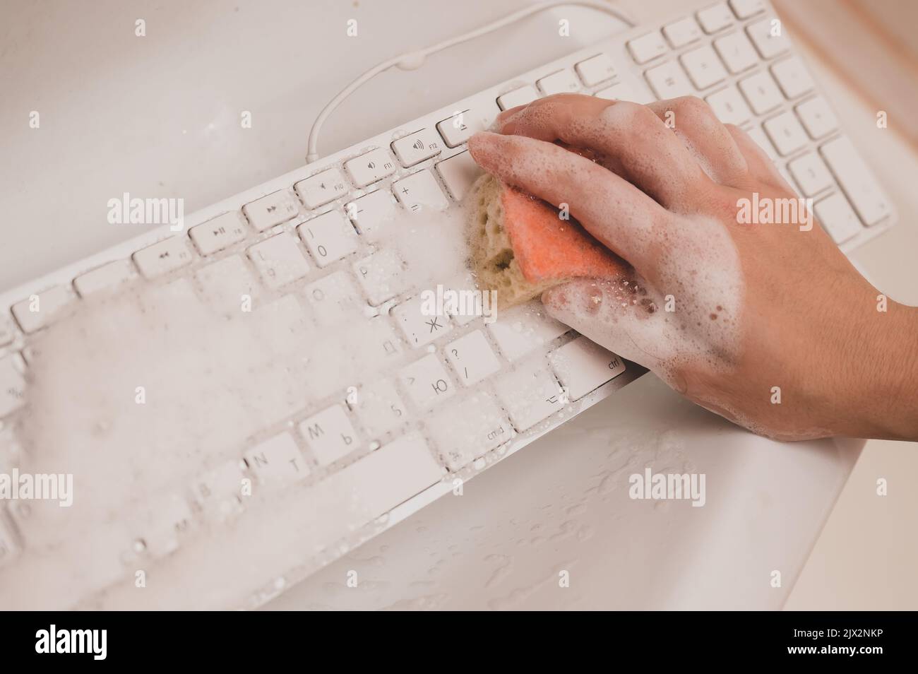 Woman washing white computer keyboard with a sponge with foam Stock