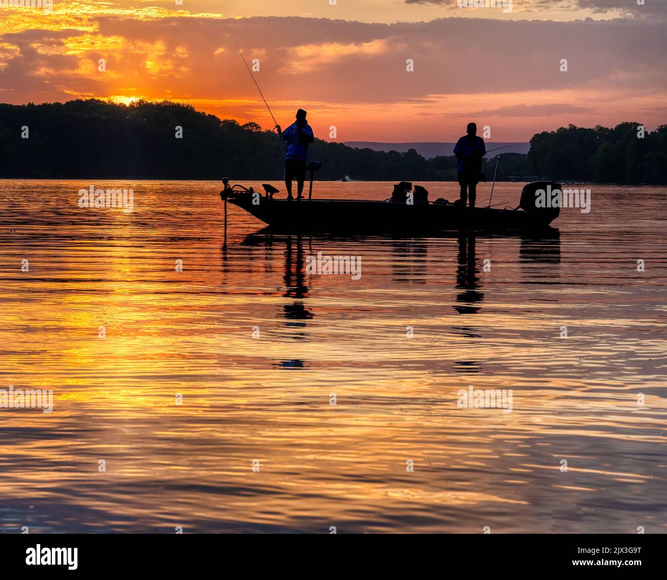 Two men bass fishing in a bass boat on Tims Ford lake in Tennessee with early morning sunrise silhouette. Stock Photo