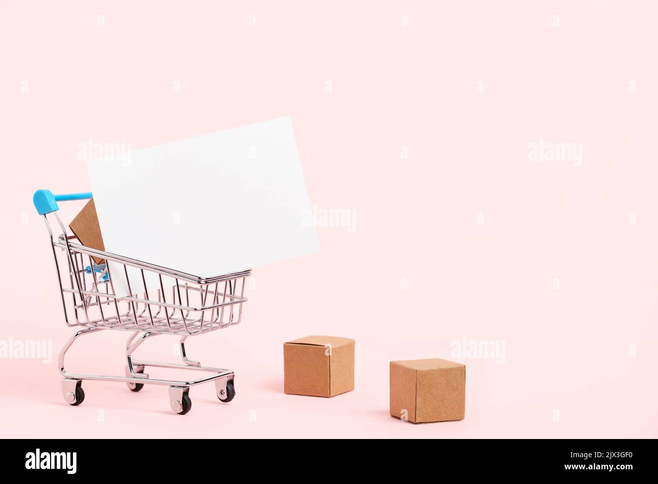 Shopping cart with cardboard boxes and a blank white paper poster on a pastel pink background. Minimalist design with copy space. Concepts: market dea Stock Photo