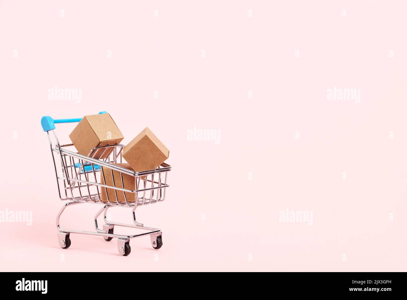 Shopping cart with cardboard boxes on a pastel pink background. Bright minimalist design with copy space. Concepts: market sales, seasonal discounts, Stock Photo