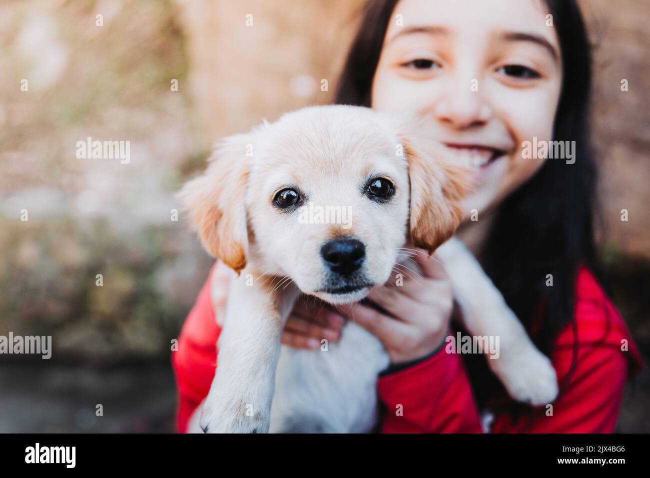 Smiling little girl embracing a golden retriever puppy in the park Stock Photo
