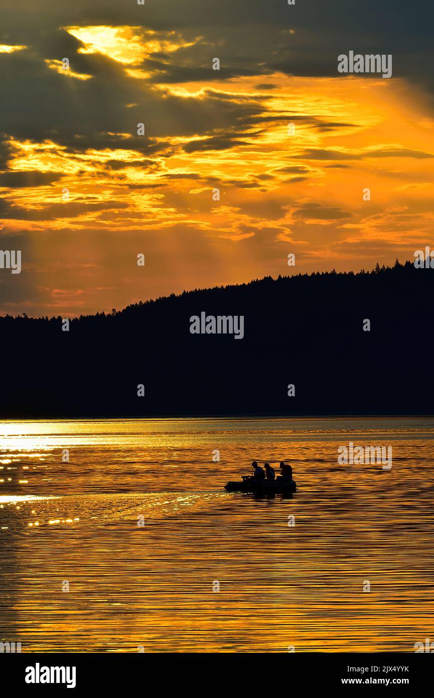Fishermen fishing from a rubber boat on golden colored water in the Stewart channel between Vancouver Island and the Gulf Islands in the early morning Stock Photo
