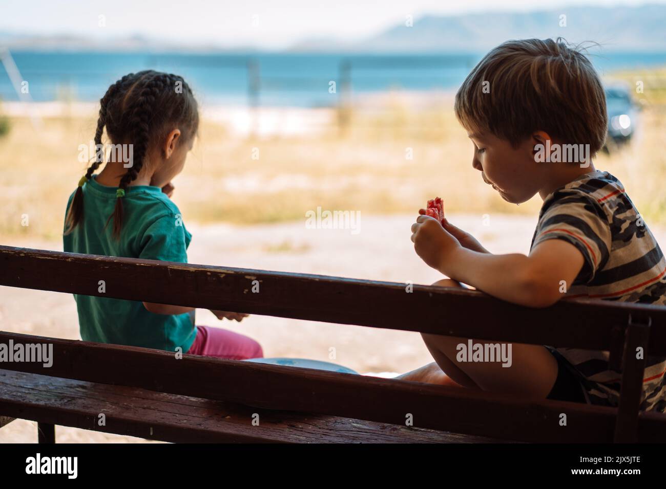 Children sitting on a bench eat watermelon in front of the sea Stock ...
