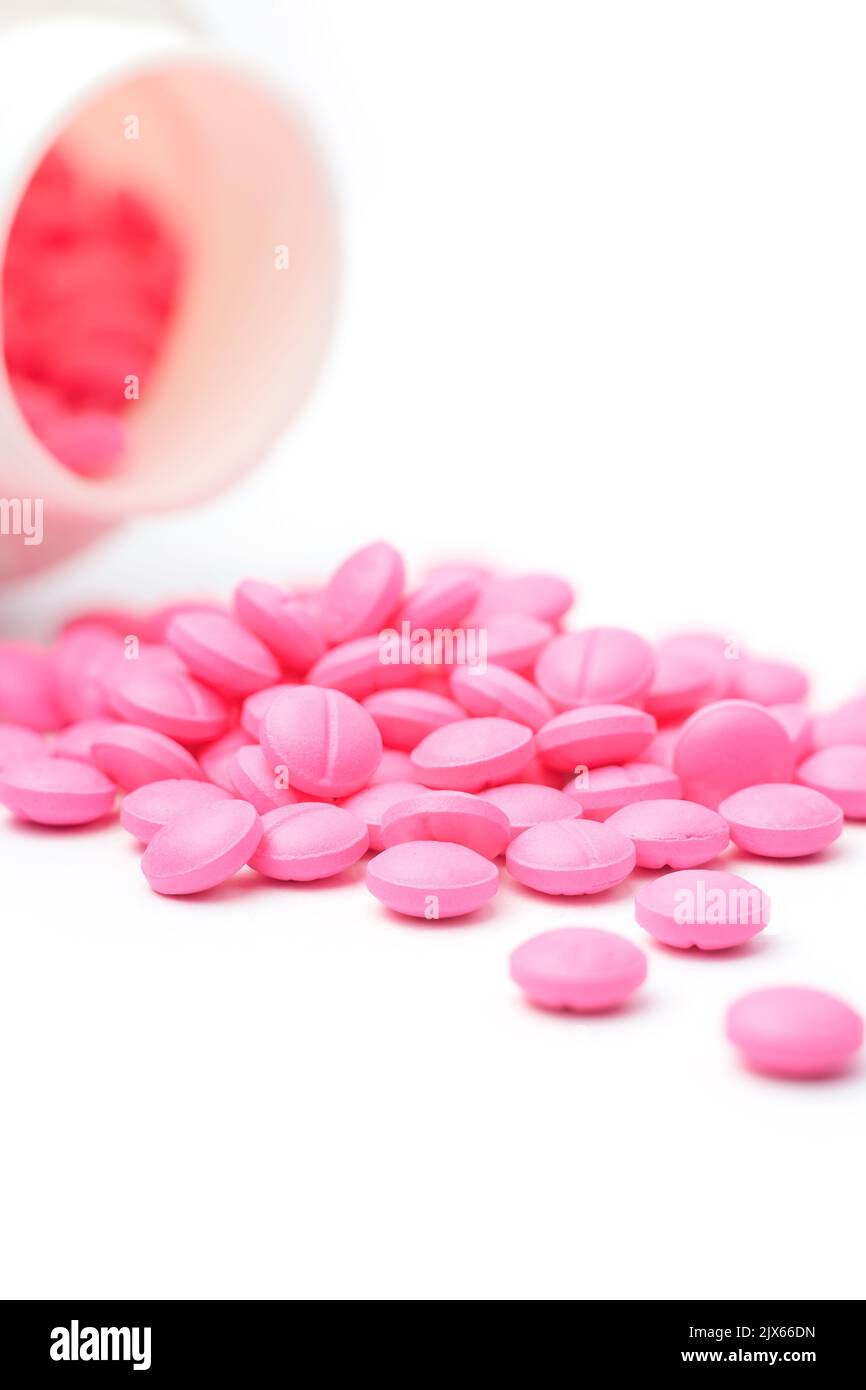 pink round pills or tablets scattered on white background from its bottle or container, medical drugs taken soft-focus with copy space Stock Photo
