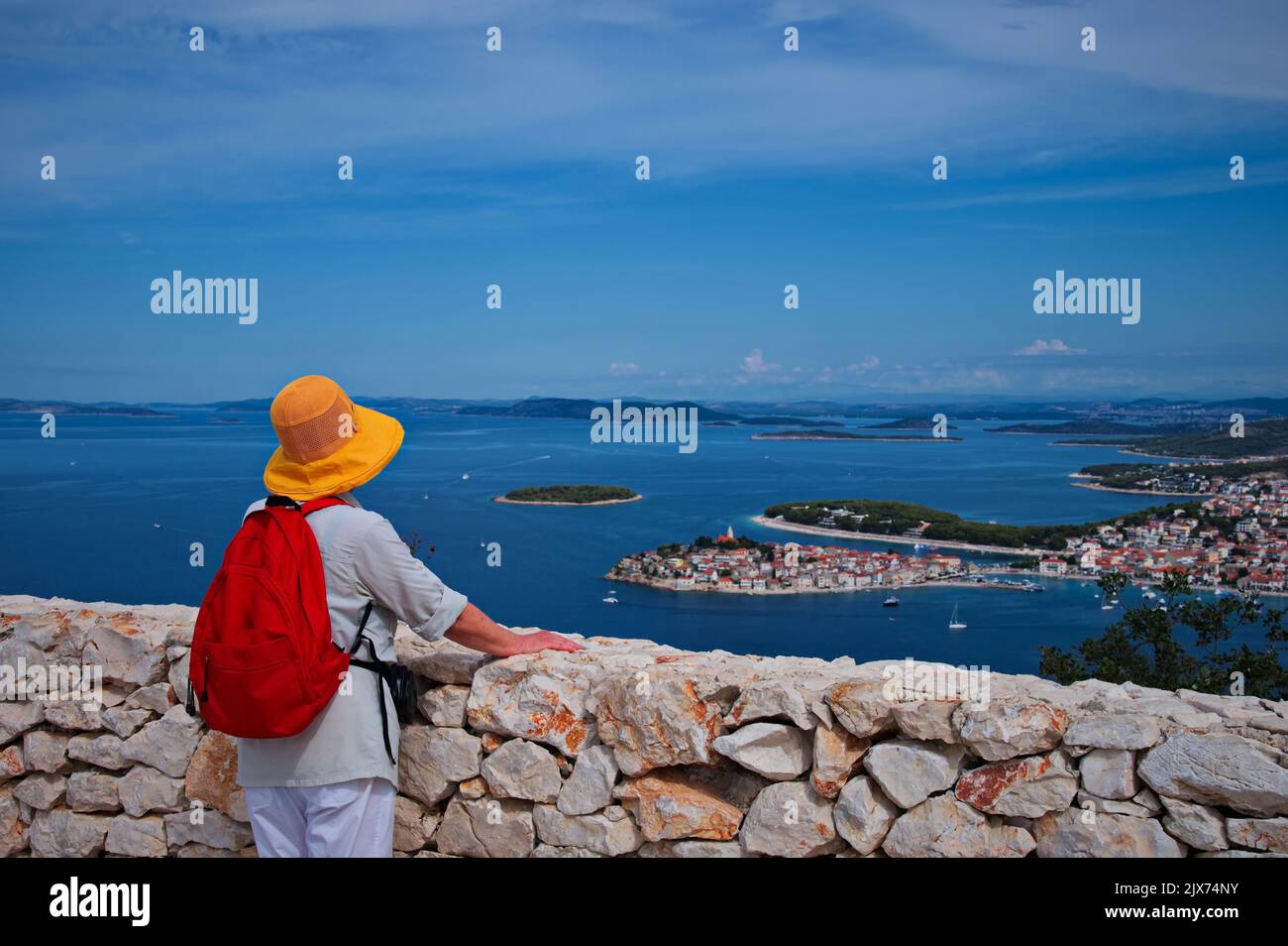 Senior woman standing on the hill looking at cityscape of Mediterranean town over the sea Stock Photo