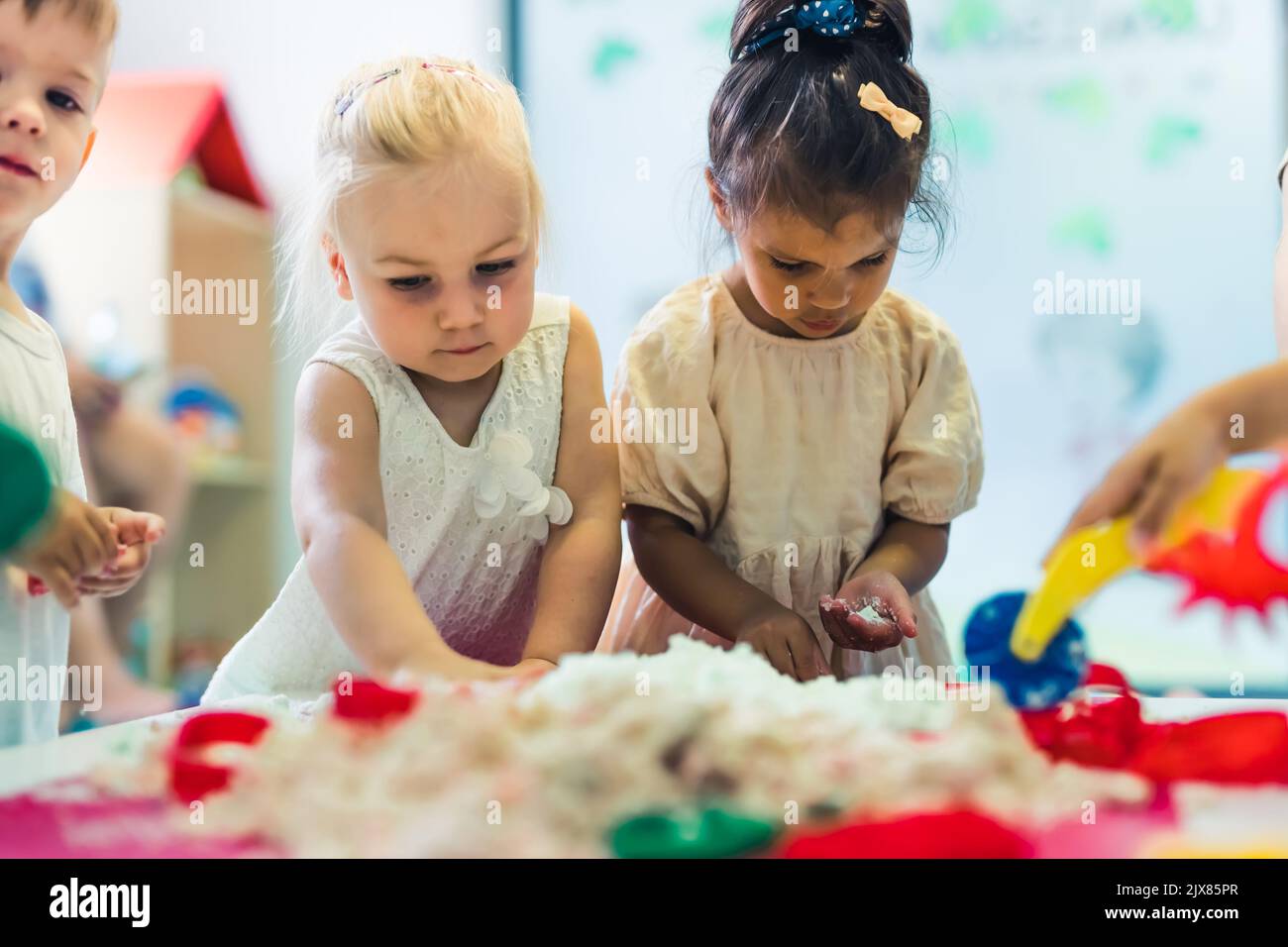 Relaxing sensory play with moldable kinetic sand at nursery school. Toddlers having fun around the table using different tools for sculpting sand such as colorful and textured rolling pins, cutters, silicone shape cases. Fine motor skills and creative development . High quality photo Stock Photo