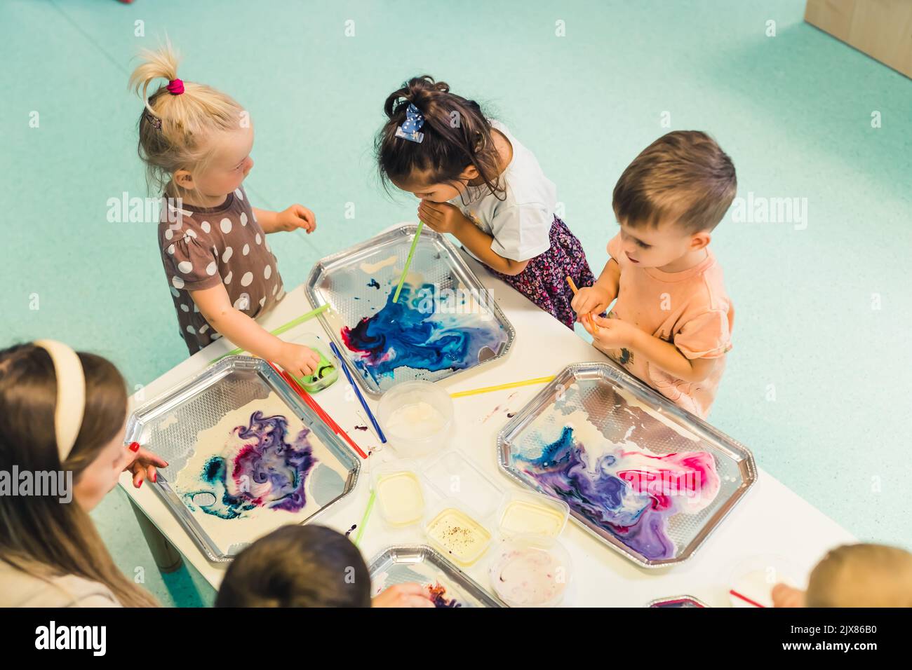 Multicultural group of children at the nursery school milk painting, using pigments for color. Finger paint. High quality photo Stock Photo