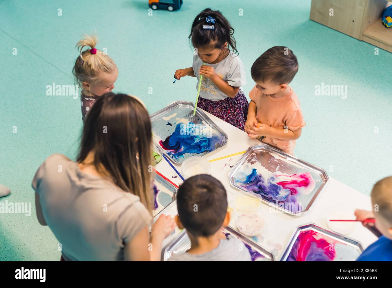 Multicultural group of children at the nursery school. Ethnic little girl milk painting, using pigments for color. Finger paint. High quality photo Stock Photo