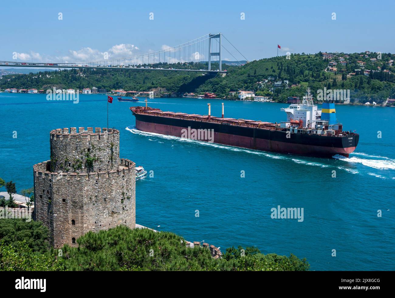An ocean liner sails along the Bosphorus Strait past Rumeli Hisari (Fortress) towards the Fatih Sultan Mehmet Bridge at Istanbul in Turkey. Stock Photo