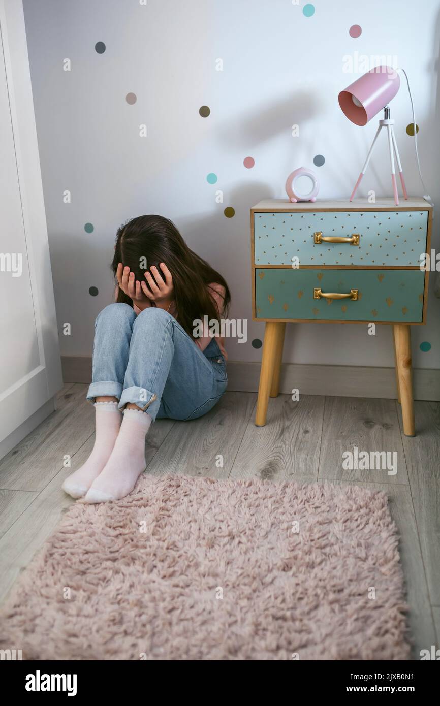 Unrecognizable little girl covering her face with hands sitting on the floor Stock Photo