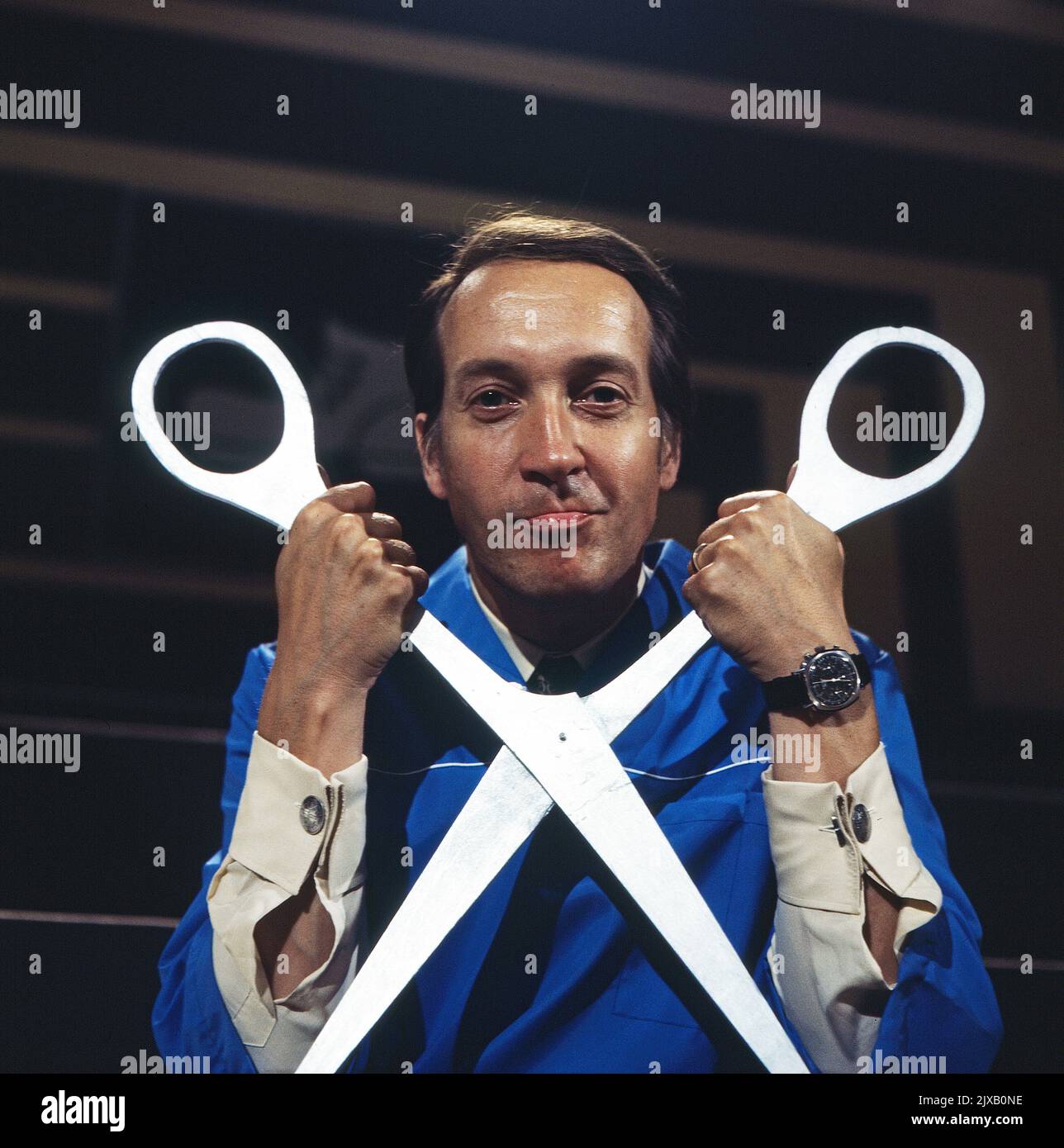 Das Kreuzworträtselspiel, Spielshow, Deutschland 1971, Mitwirkende: Ernst Stankovski als Friseur im blauen Hemd mit übergroßer Schere. Stock Photo