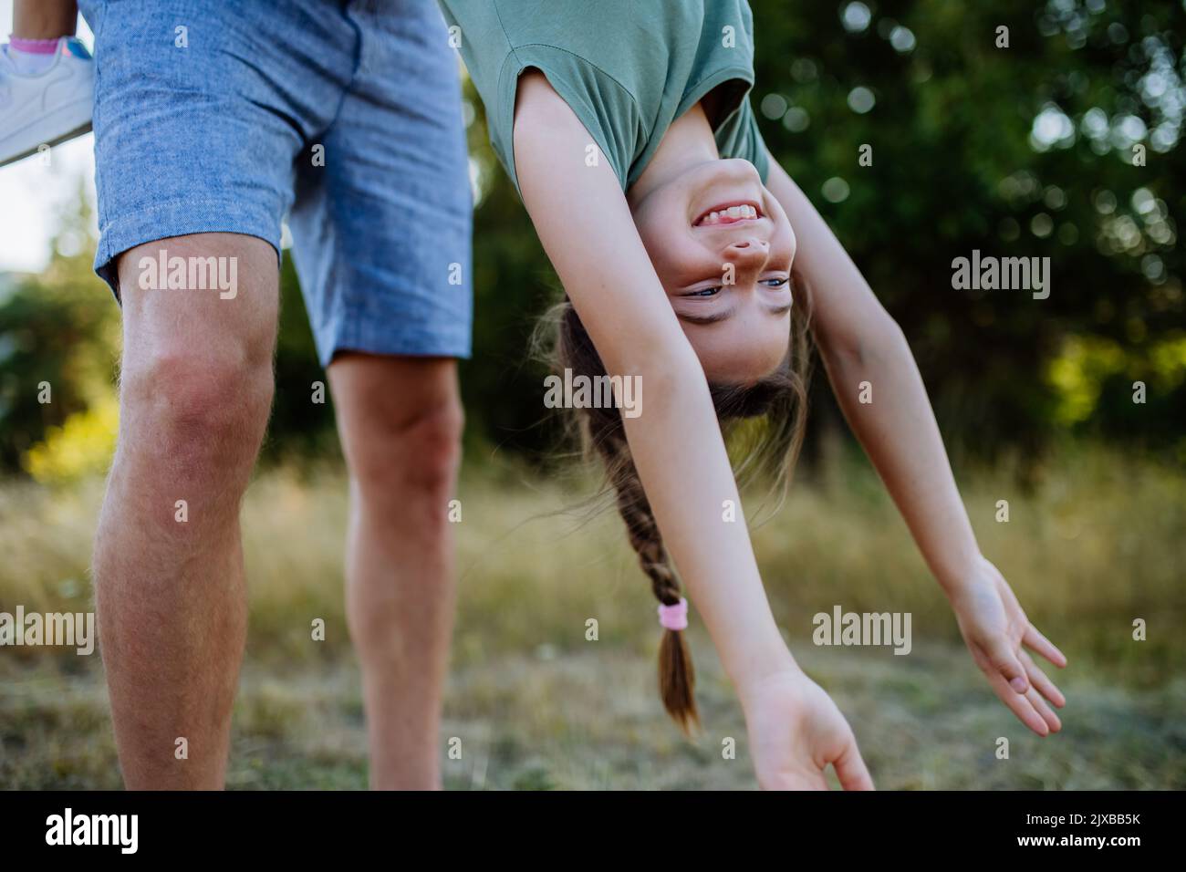 Father swing her daughter, holding her upside down, having fun together in nature. Stock Photo