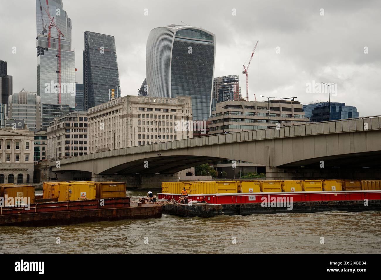 The City of London with barges laden with containers on the river Thames. Stock Photo