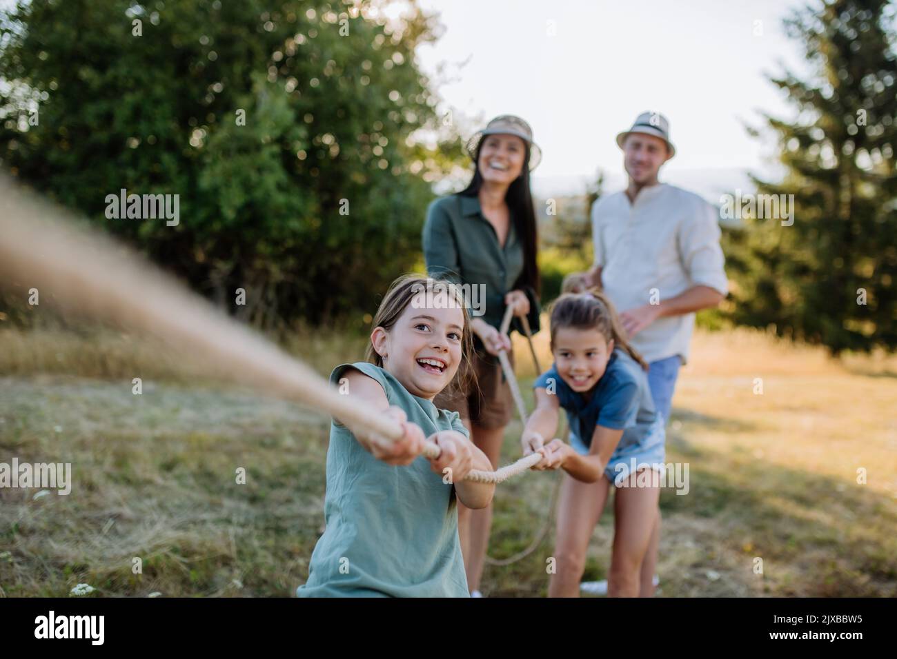 Young family with happy kids having fun together outdoors pulling rope in summer nature. Stock Photo