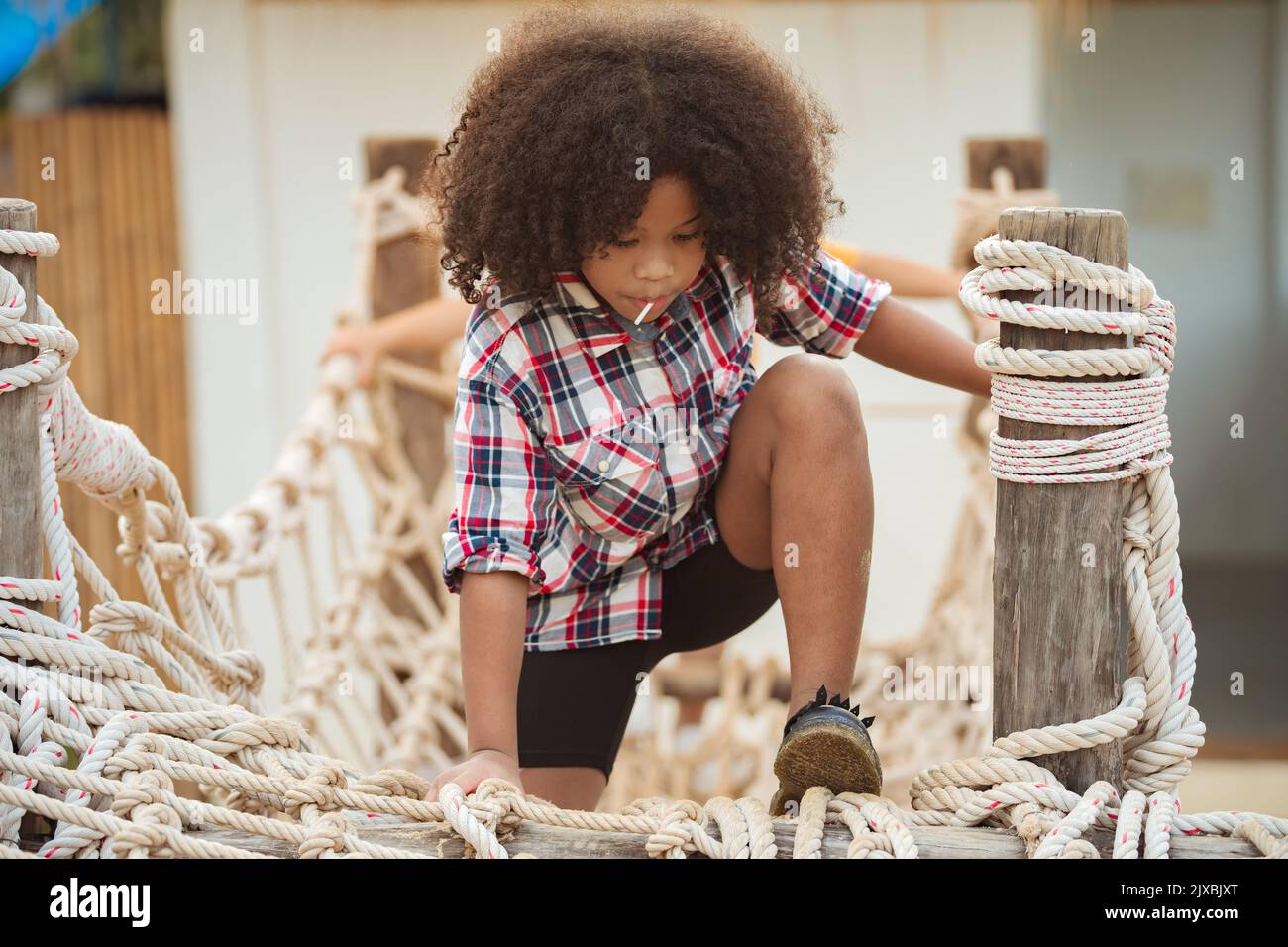 African american kid girl playing on a Rope-ladder web in a playground. Stock Photo