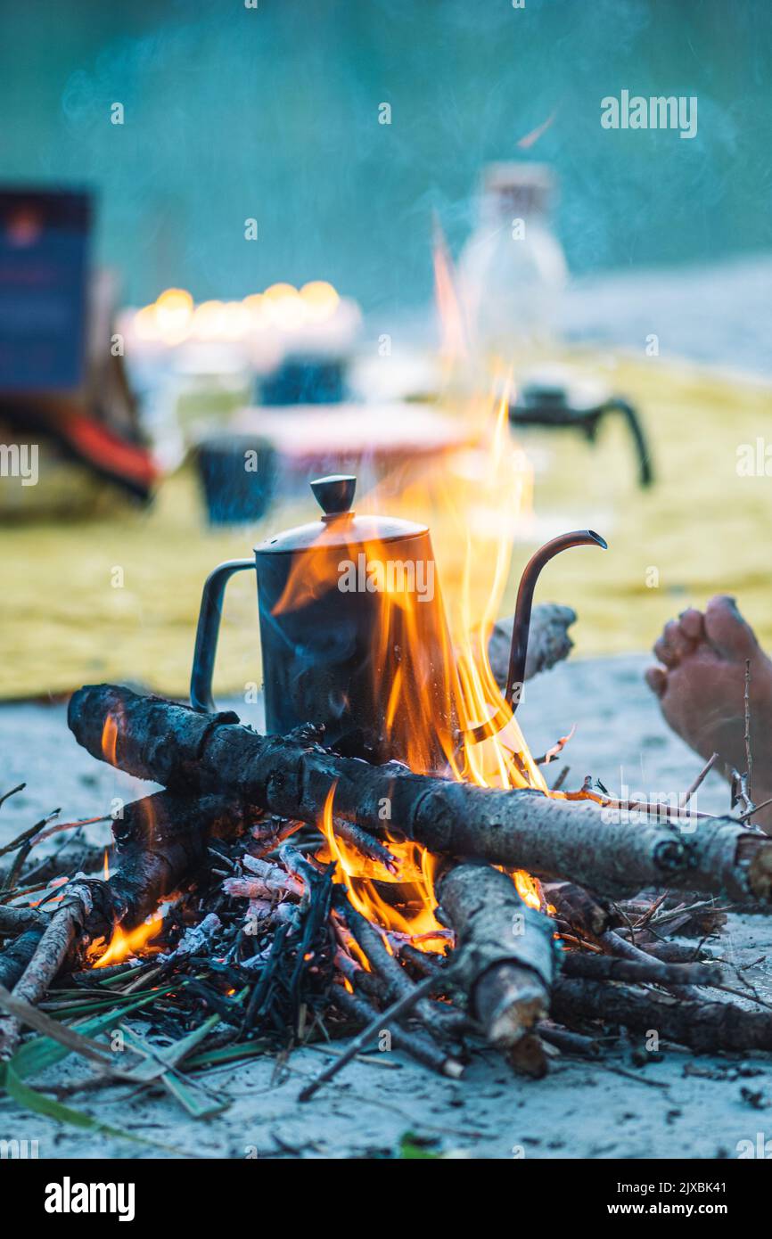 Preparing coffee or tea on a bonfire with branches and flames outdoor in the nature, vertical Stock Photo