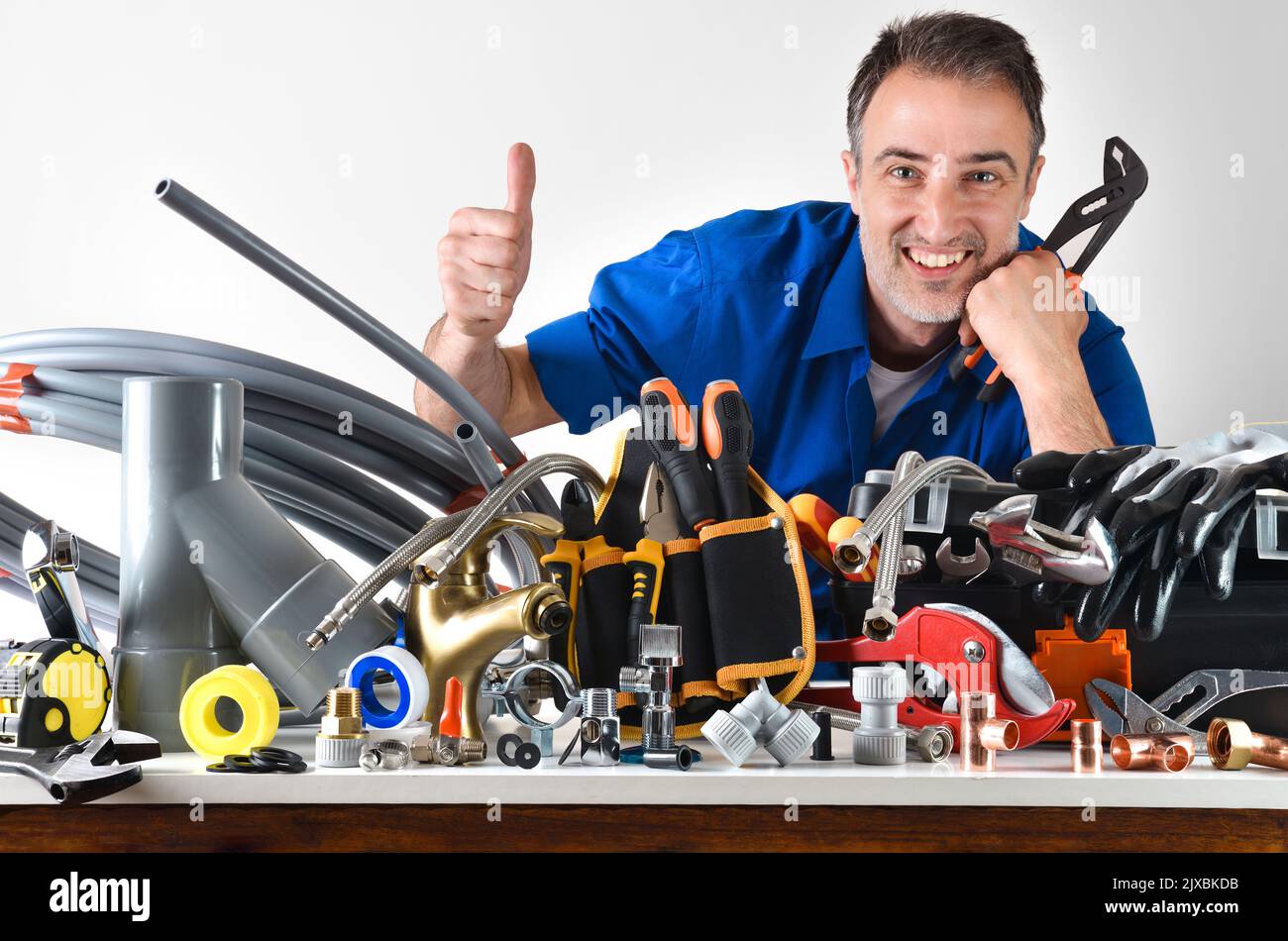 Sample of plumbing materials and tools on workbench with plumber with ok sign and white isolated background. Front view. Horizontal composition. Stock Photo