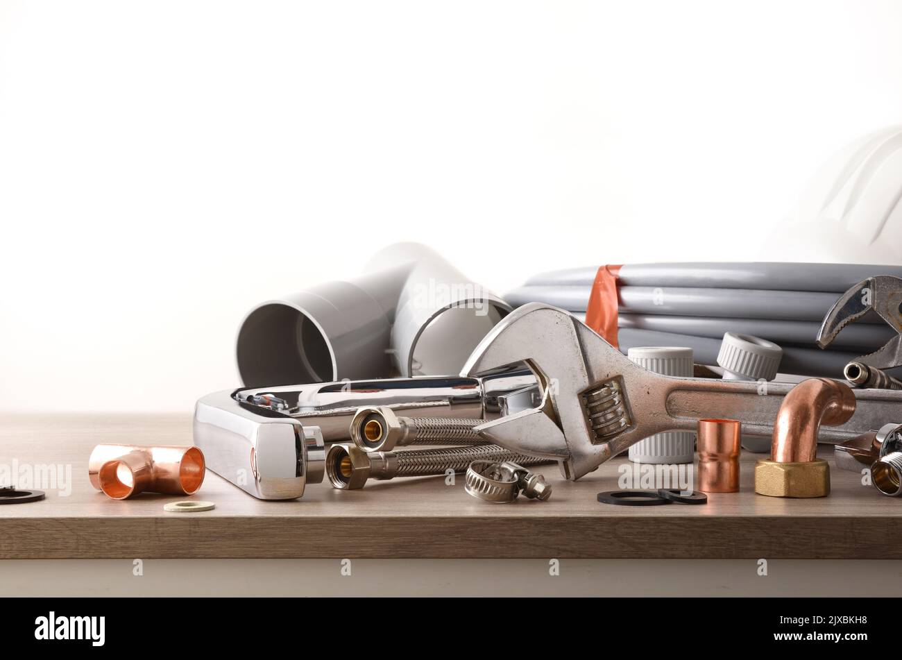Plumbing material and tools on wooden bench and white isolated background. Front view. Horizontal composition. Stock Photo