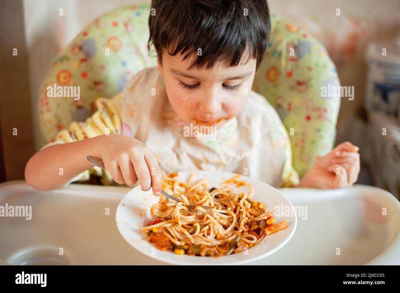 Child eating spaghetti with vegetables. Kid having fun eating. Brown