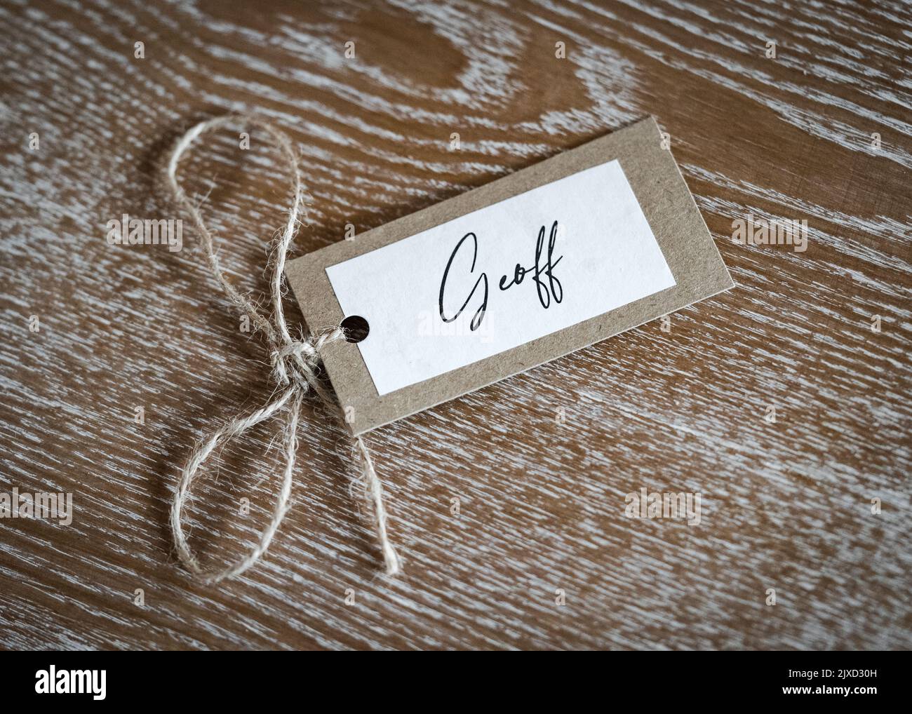 Personalised name Geoff place card with string label beautiful crafted placard.  Laid on solid oak wooden table named ticket tag. Stock Photo