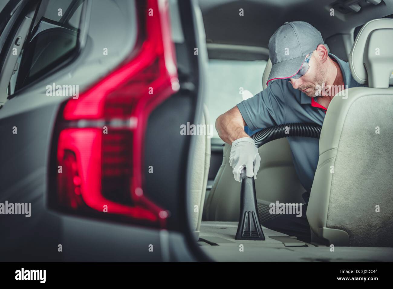 Caucasian Auto Detailer Precisely Vacuuming Folded Down Car Back Seat