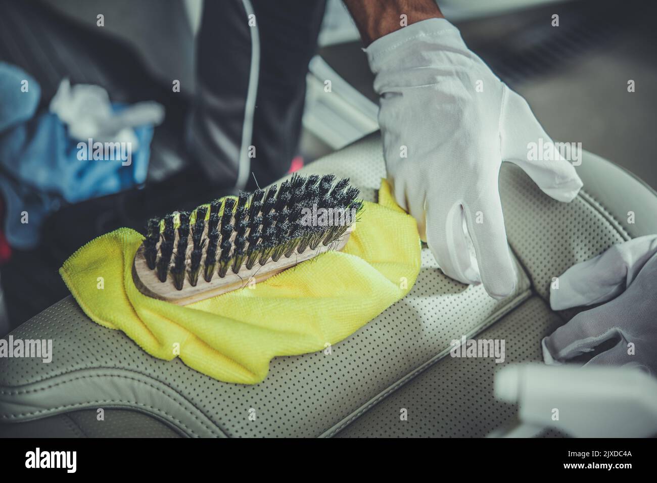 Vehicle Cleaner in White Gloves Precisely Cleaning Car Leather Seats Using Cloth and Brush to Maintain Its Good Looking Interior. Professional Auto De Stock Photo