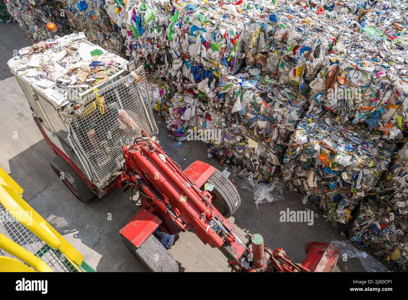 Waste Sorting Station Worker Driving Bulldozer Track Loader Arranging Storage of Bales of Compressed Garbage. Stock Photo