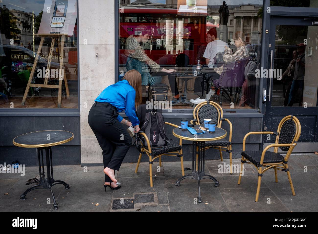 A woman changes into her work shoes outside a Caffe Nero on Trafalgar