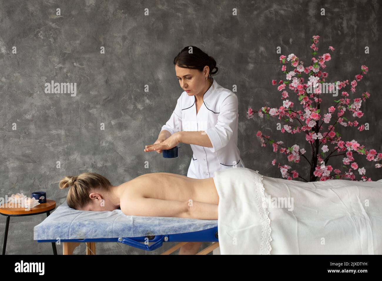 Serious professional female medical physiotherapist do massage, pouring hot wax on back of patient lying down on table  Stock Photo