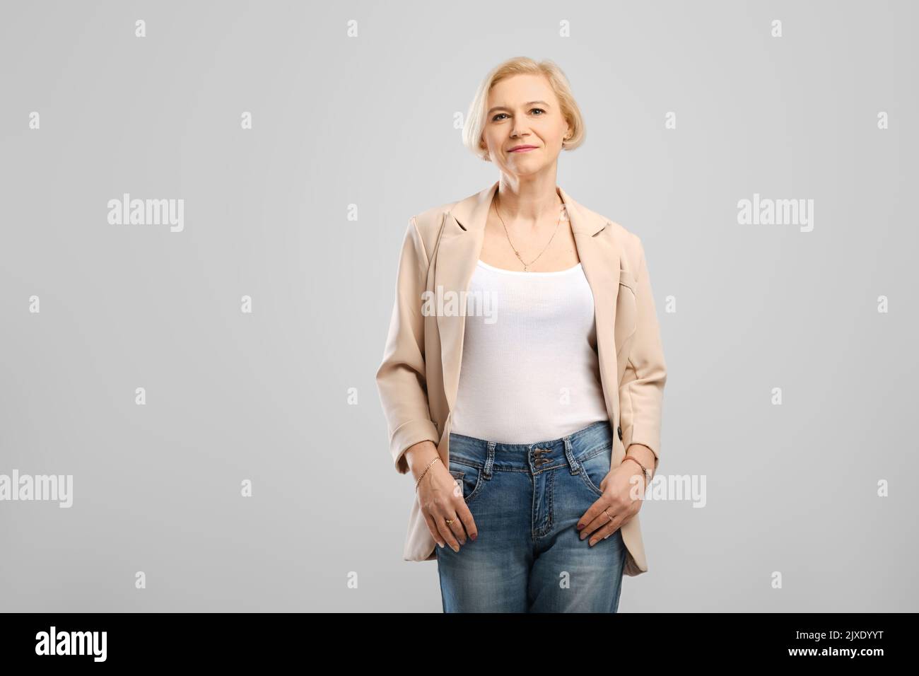 Confident middle age woman standing with arms in the pockets looking at camera at gray background Stock Photo