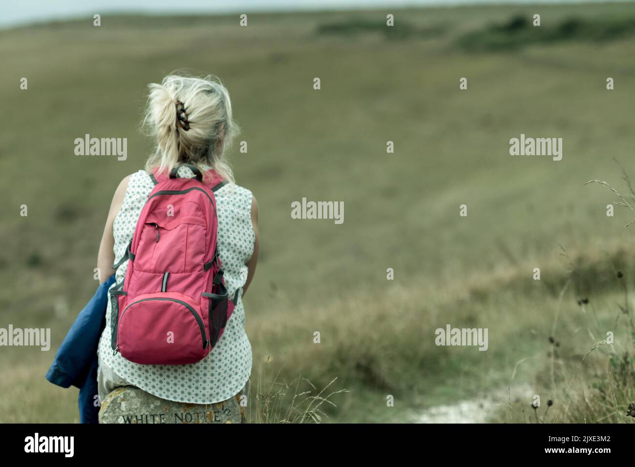 Woman sitting on a milestone with a backpack looking at the path ahead Stock Photo